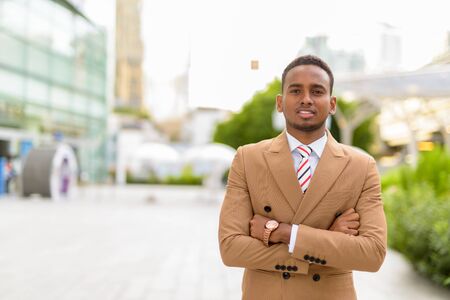 Happy young handsome African businessman with arms crossed in the city outdoorsの写真素材