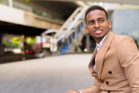 Happy young handsome African businessman thinking in the city outdoorsの写真素材