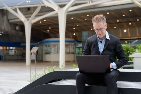 Mature businessman with eyeglasses using laptop in the city streets outdoorsの写真素材