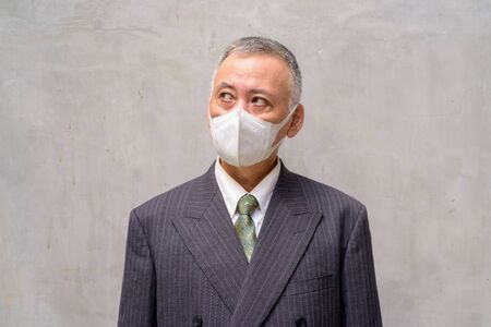 Face of mature Japanese businessman with mask thinking outdoorsの写真素材