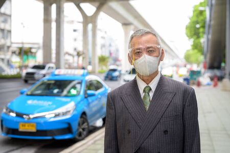 Mature Japanese businessman with mask and face shield at the taxi stationの写真素材