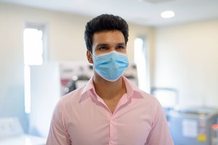 Young Indian businessman with mask thinking at the laundromat indoorsの写真素材