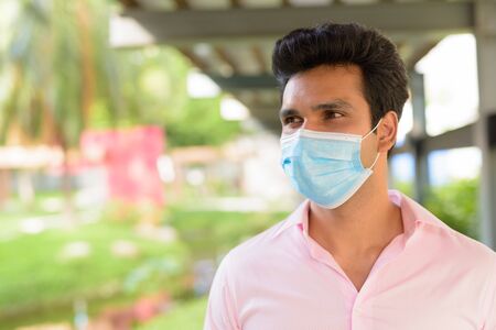 Face of young Indian businessman wearing mask and thinking at the parkの写真素材