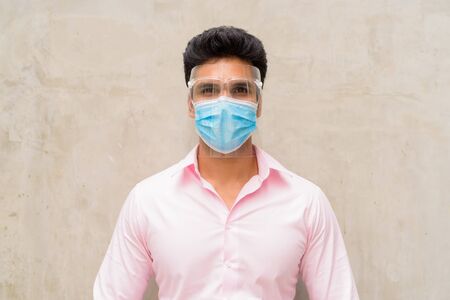 Young Indian businessman wearing mask and face shield for protection from corona virus outbreak outdoorsの写真素材