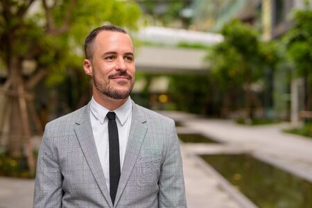 Handsome Hispanic bald bearded businessman thinking with nature in the city outdoorsの写真素材