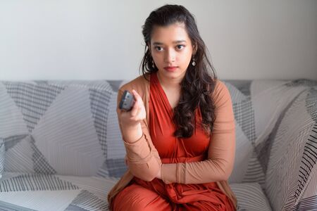Young Indian woman looking serious while watching tv in the living room at homeの写真素材