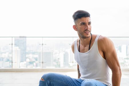 Happy young handsome bearded Persian man thinking in the city outdoorsの写真素材