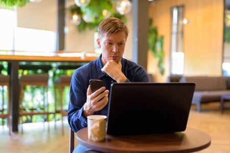 Young handsome businessman using phone and laptop at the coffee shopの写真素材
