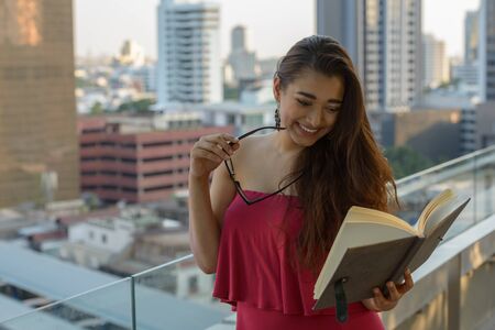Happy young beautiful Indian woman reading book against view of the cityの写真素材