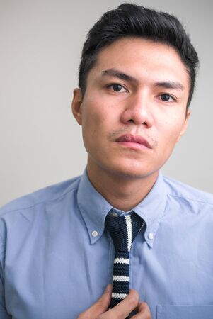 Face of young handsome Asian businessman fixing tieの写真素材