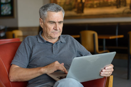 Handsome senior man using laptop and relaxing at home indoors