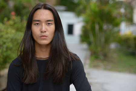 Face of young Asian man with long hair at the parkの写真素材