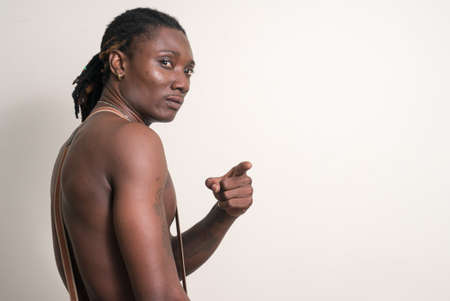 Young handsome muscular African man with dreadlocks pointing finger and looking back shirtlessの写真素材