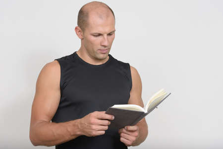 Portrait of young handsome bald man reading book and ready for gymの写真素材