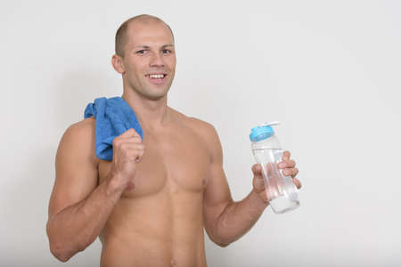 Happy young muscular bald man with face towel and water bottle shirtlessの写真素材
