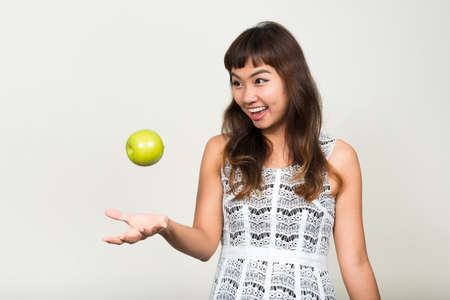Portrait of happy young beautiful Asian woman throwing appleの写真素材