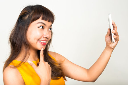 Profile view of happy young beautiful Asian woman taking selfie