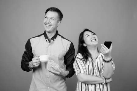 Young handsome businessman and mature Asian businesswoman against gray backgroundの写真素材