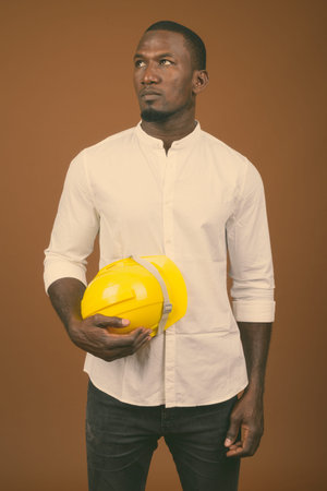 Handsome African businessman with hardhat against brown background
