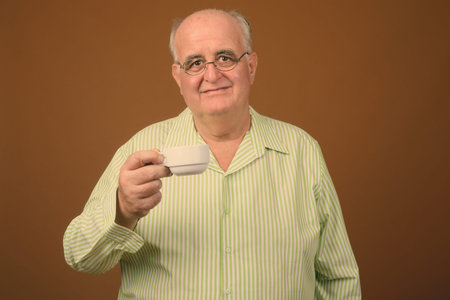 Overweight senior man wearing eyeglasses against brown background