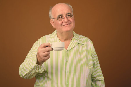 Overweight senior man wearing eyeglasses against brown background