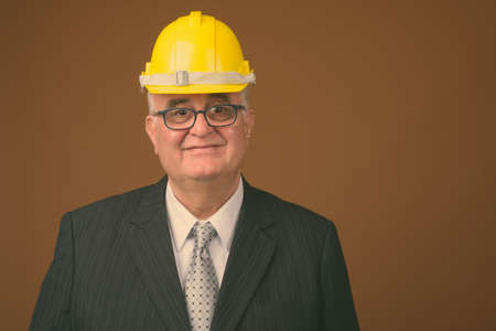Overweight senior businessman with hardhat against brown backgroundの写真素材