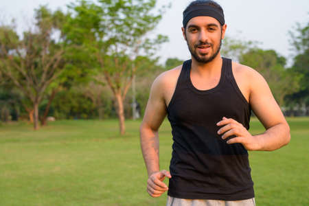 Young handsome bearded Indian man jogging at the parkの写真素材