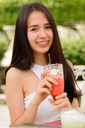 Happy young beautiful Asian woman with milkshake at the coffee shop outdoorsの写真素材