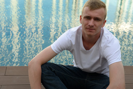 Portrait of young man with blond hair by the swimming pool outdoors
