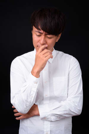 Young handsome Asian businessman against black backgroundの写真素材