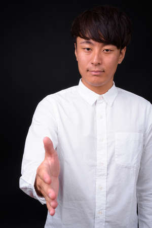 Young handsome Asian businessman against black backgroundの写真素材