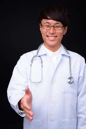 Young handsome Asian man doctor against black backgroundの写真素材