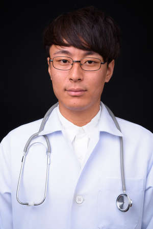 Young handsome Asian man doctor against black backgroundの写真素材