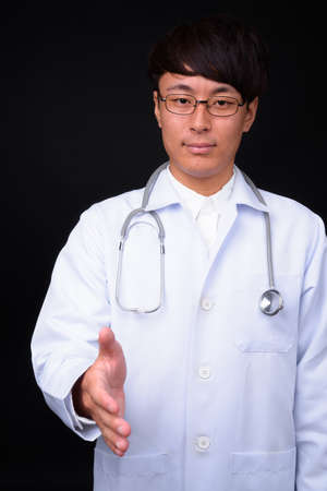 Young handsome Asian man doctor against black backgroundの写真素材