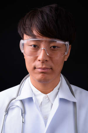 Young handsome Asian man doctor wearing protective glasses against black backgroundの写真素材