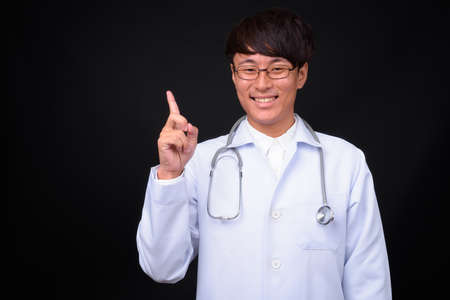 Young handsome Asian man doctor against black backgroundの写真素材