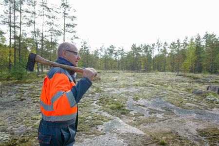 Profile view of happy mature handsome man holding ax in the forest