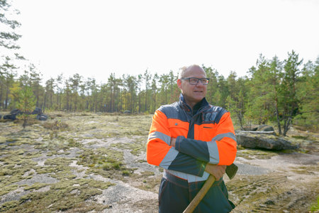 Portrait of happy mature handsome man thinking and holding ax in the forest