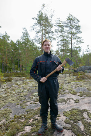 Portrait of happy young handsome man holding ax in the forest