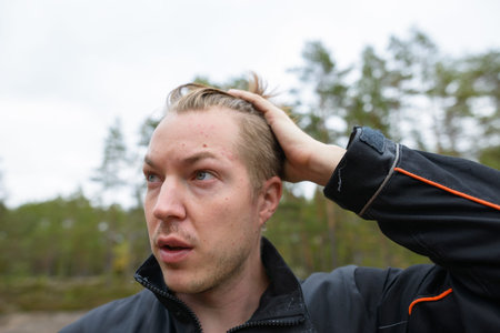 Face of young handsome man brushing hair back while thinking in the forest
