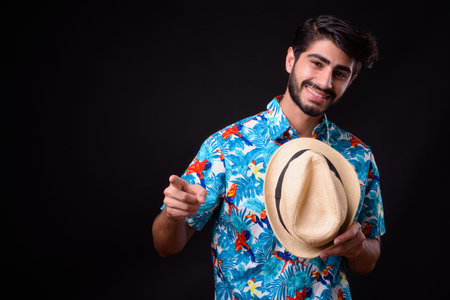 Young handsome bearded Persian tourist man ready for vacation against black background