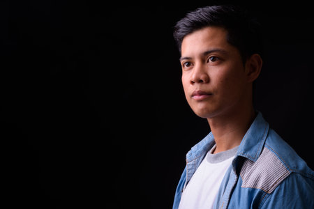 Portrait of young Asian man against black background