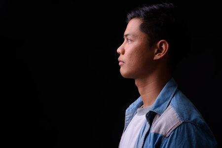 Portrait of young Asian man against black background