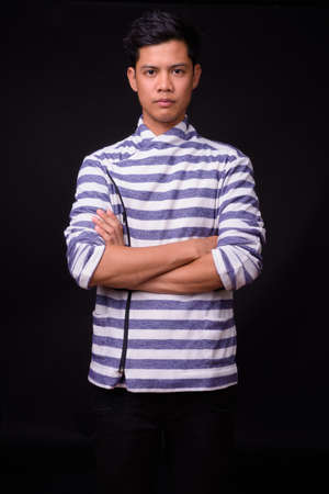 Portrait of young Asian man against black backgroundの写真素材