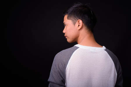 Portrait of young Asian man against black backgroundの写真素材