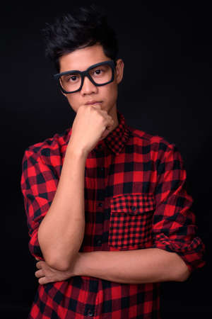 Portrait of young Asian hipster man against black backgroundの写真素材