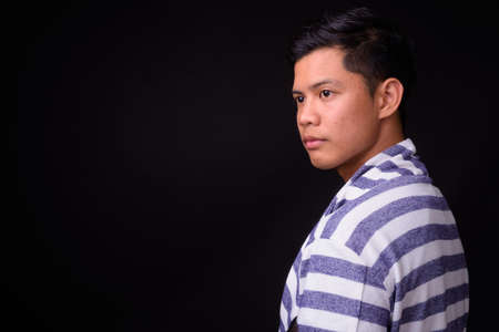 Portrait of young Asian man against black backgroundの写真素材