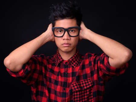 Portrait of young Asian hipster man against black backgroundの写真素材