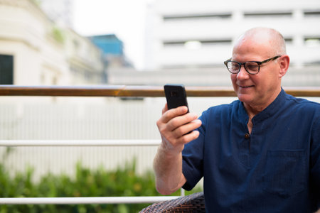 Happy senior handsome tourist man using phone and relaxing with nature outdoors
