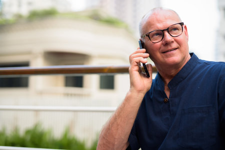 Happy senior handsome tourist man talking on the phone and relaxing with nature outdoors